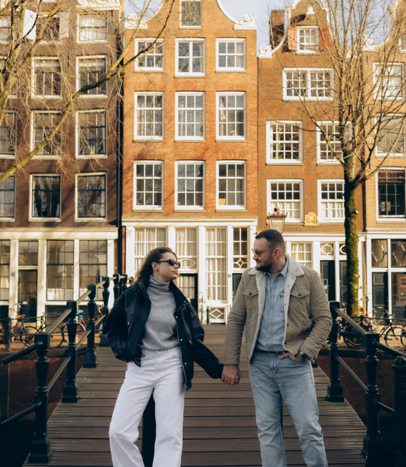 Couple holding hands on a bridge with gabled houses behind, Amsterdam