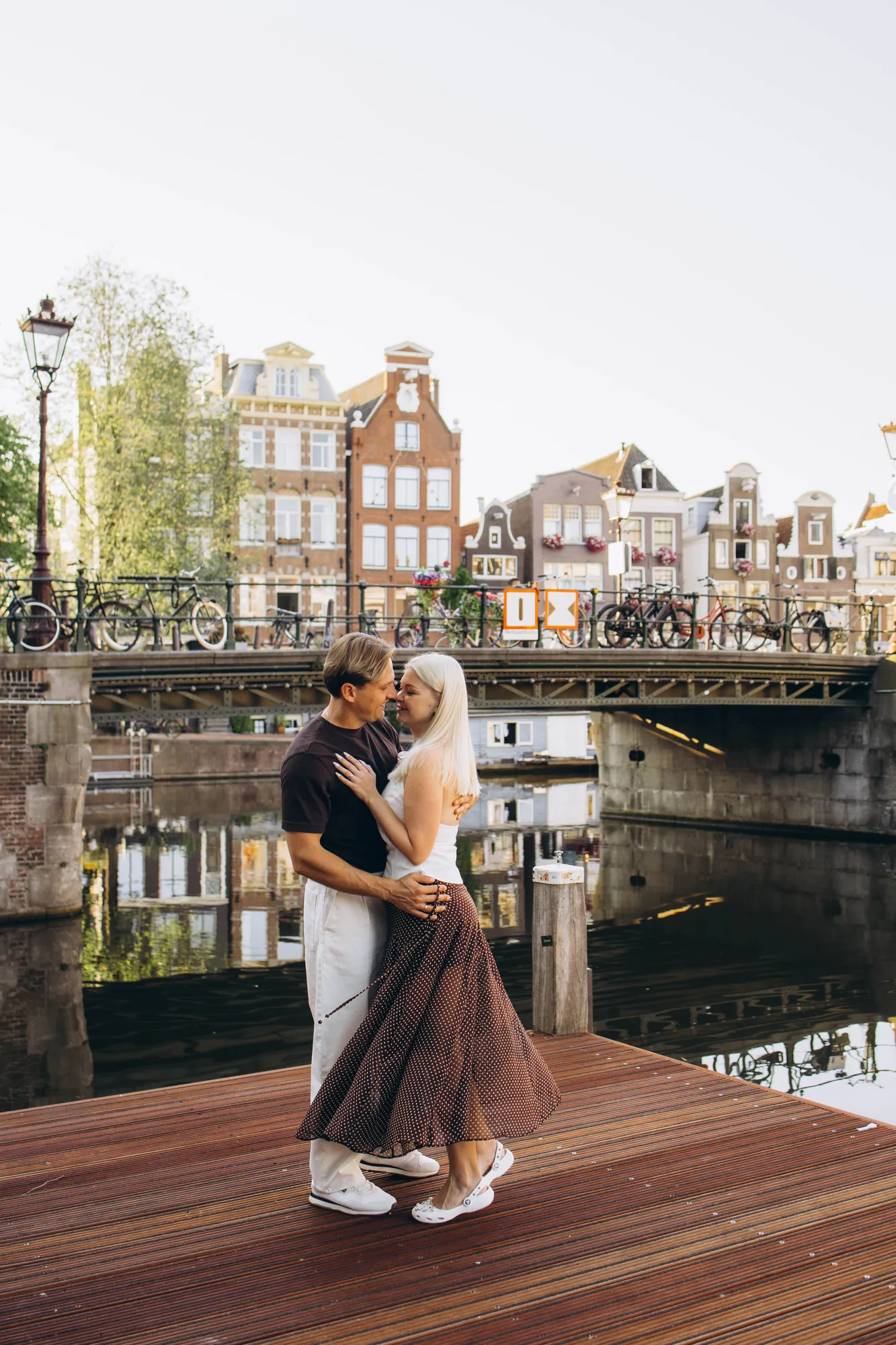 Couple dancing on a wooden canal pontoon with a bridge and gabled houses behind, Amsterdam