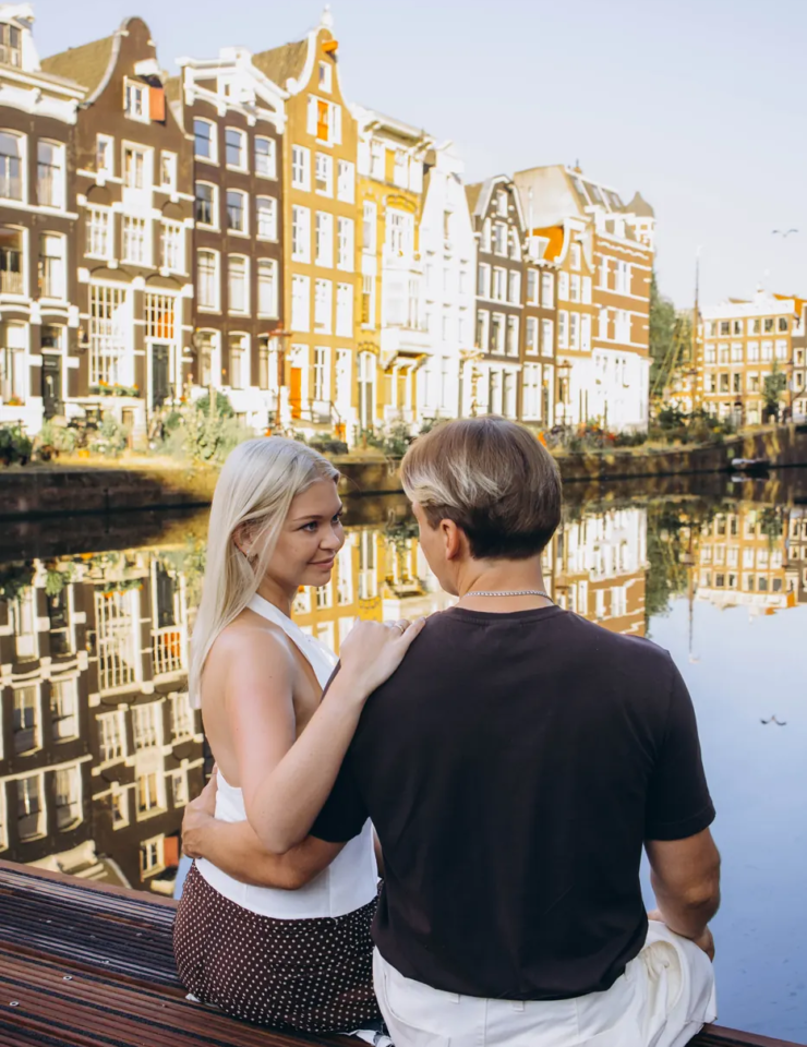 Couple sitting on a wooden pontoon, gabled canal houses reflected in the water, Amsterdam