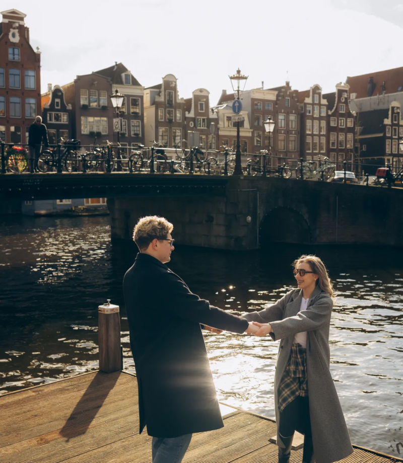 Couple dancing on a pontoon with sunlit water and canal houses behind, Amsterdam