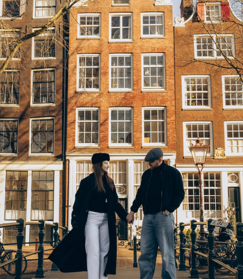 Couple walking on a canal bridge in front of gabled houses, Amsterdam