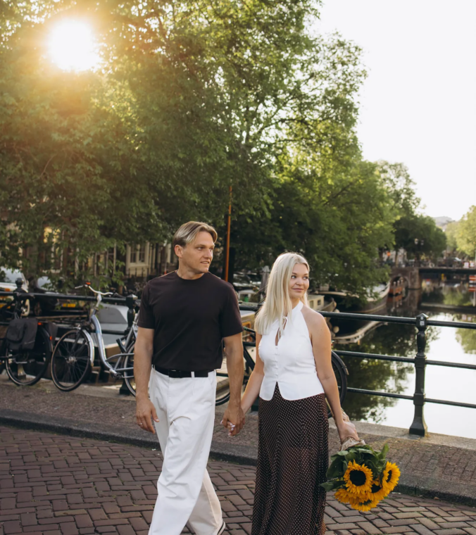 Couple walking along a canal holding sunflowers in low morning sun, Amsterdam