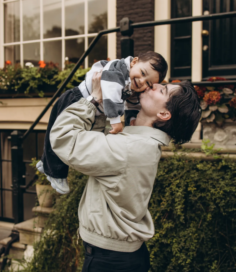 Father lifting his laughing toddler beside a green hedge, Amsterdam