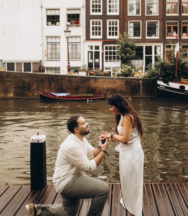 Man offering the ring on a wooden pontoon with gabled canal houses across the water, Amsterdam