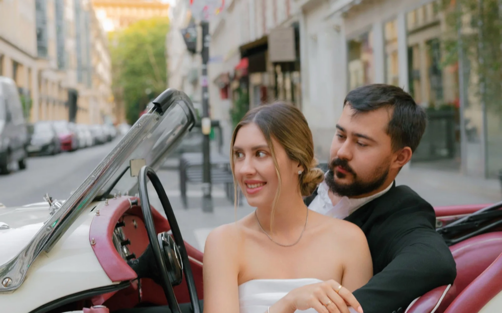Anatolii and Julia sitting in a white vintage roadster on a Paris street