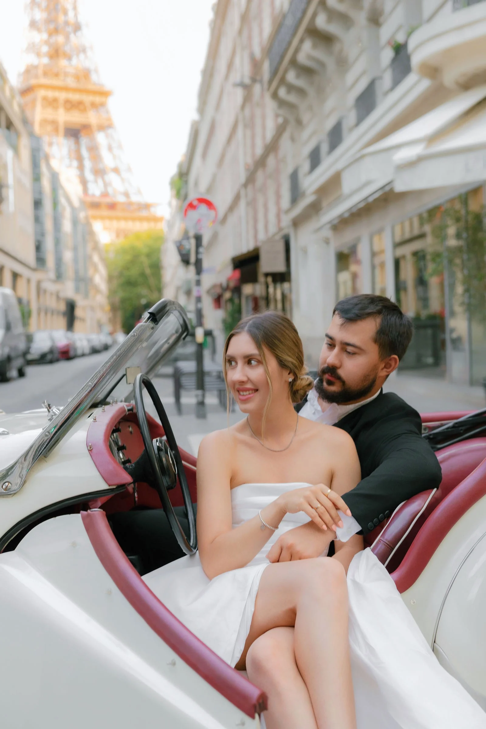 Anatolii and Julia sitting in a white vintage roadster on a Paris street