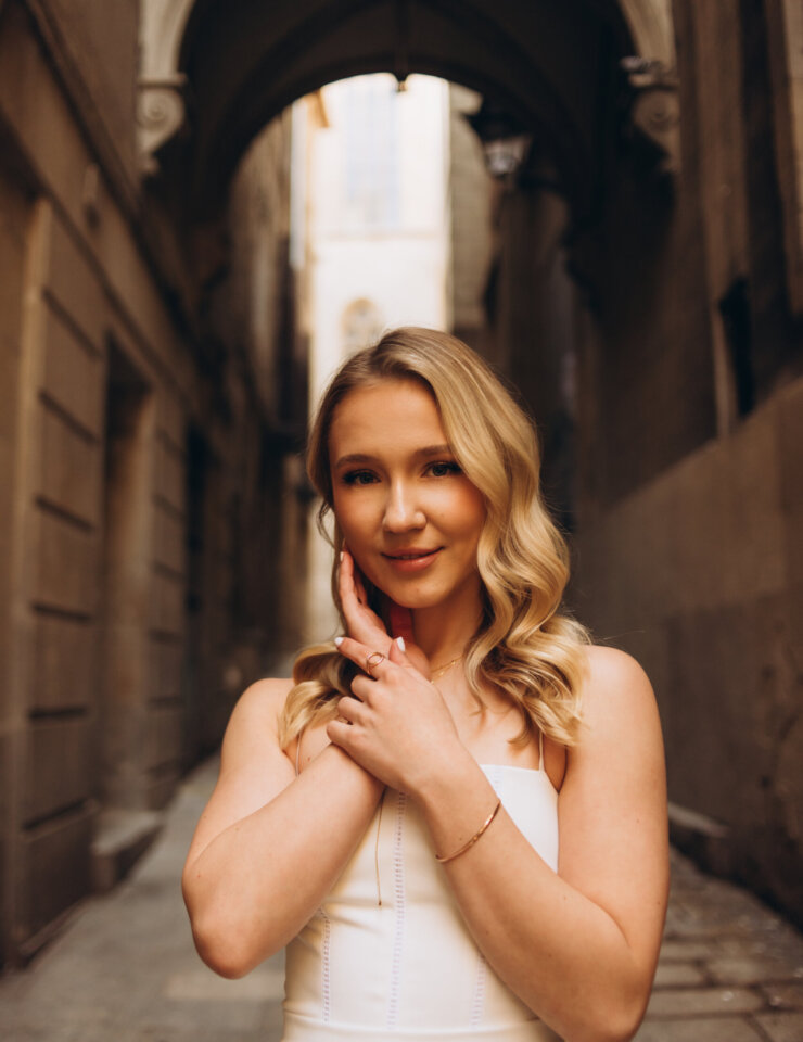 Blonde woman in a white strapless dress with hands at her face in a Gothic Quarter lane, Barcelona