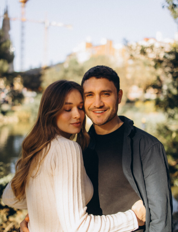 Smiling couple embracing in the park opposite the Sagrada Familia in warm morning light, Barcelona