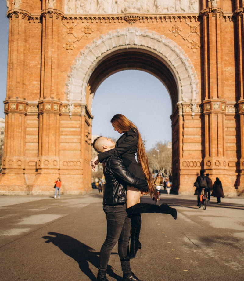 Man lifting a woman in front of the red-brick Arc de Triomf, Barcelona