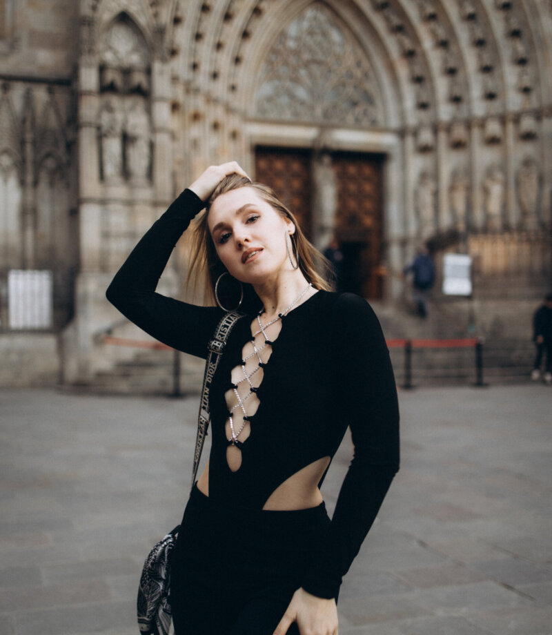 Woman in a black bodysuit with hand in her hair before the Gothic doorway of Barcelona Cathedral
