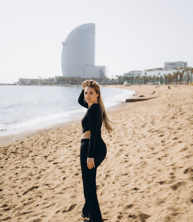 Woman in black walking on Barceloneta beach with the W Hotel sail building behind, Barcelona