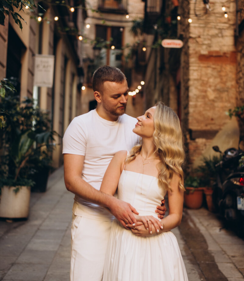 Couple in white embracing in a Gothic Quarter street strung with fairy lights, Barcelona