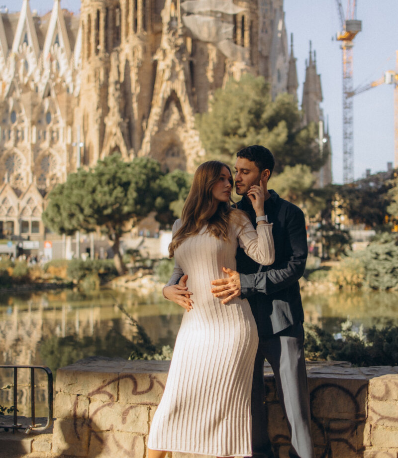 Couple in a cream knit dress and dark suit embracing in front of the Sagrada Familia, Barcelona