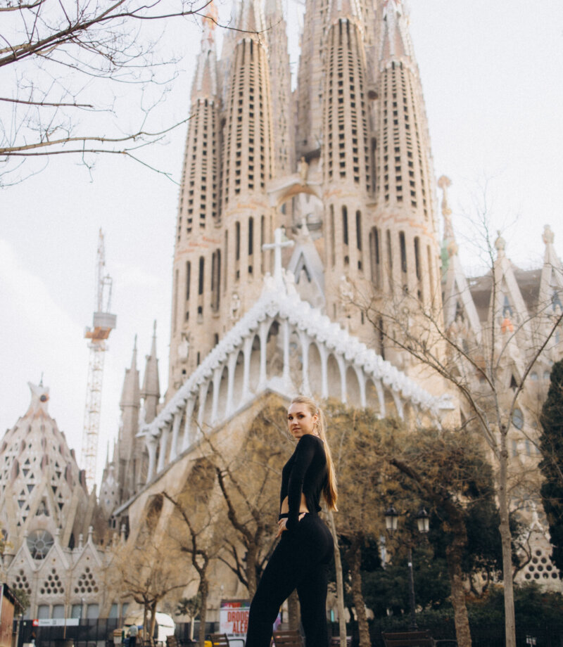 Woman in a black cut-out jumpsuit posing full length in front of the Nativity facade of the Sagrada Familia, Barcelona