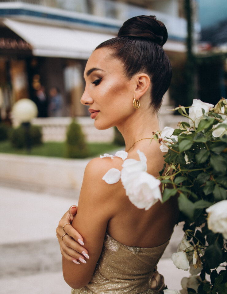 Profile of a woman in a gold strapless gown beside white roses on La Croisette, Cannes