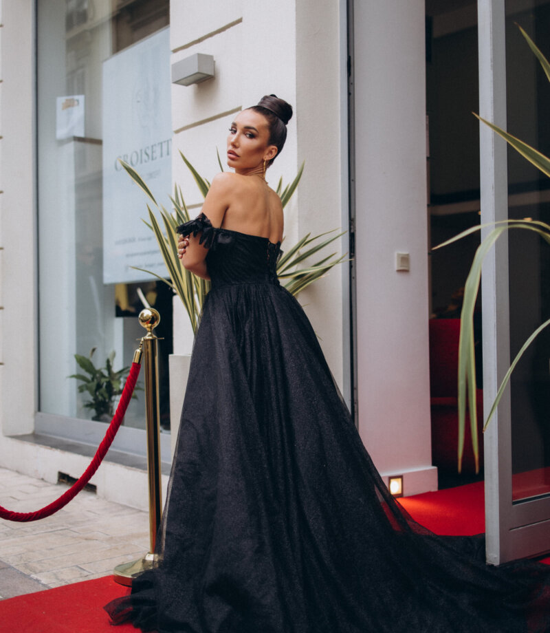 Woman in a black tulle gown on a red carpet at a hotel entrance in Cannes