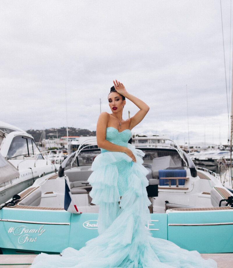 Woman in a turquoise tulle gown posing beside a teal speedboat in the Vieux Port of Cannes