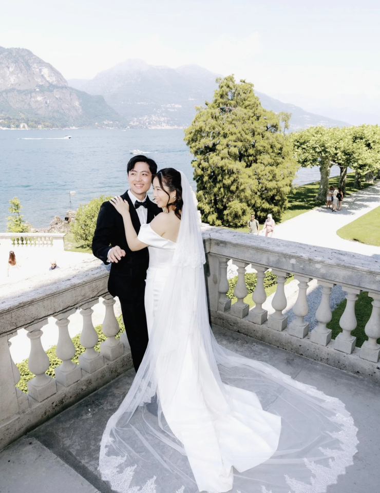 Bride and groom on a balustrade above Lake Como with mountains across the water