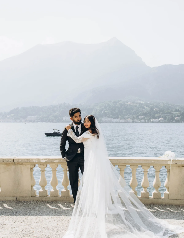 Bride and groom embracing on the stone balustrade of Villa Melzi, her cathedral veil spread over the gravel, Lake Como