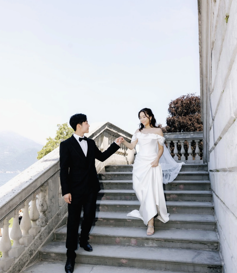 Groom leading the bride down a stone villa staircase above Lake Como