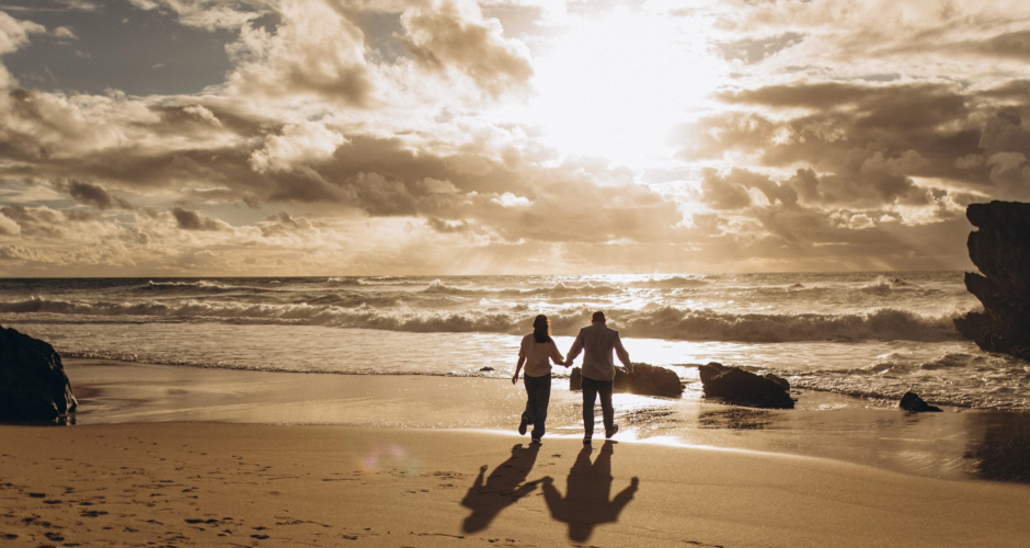 Couple walking hand in hand on an Atlantic beach under a dramatic golden sunset sky near Lisbon