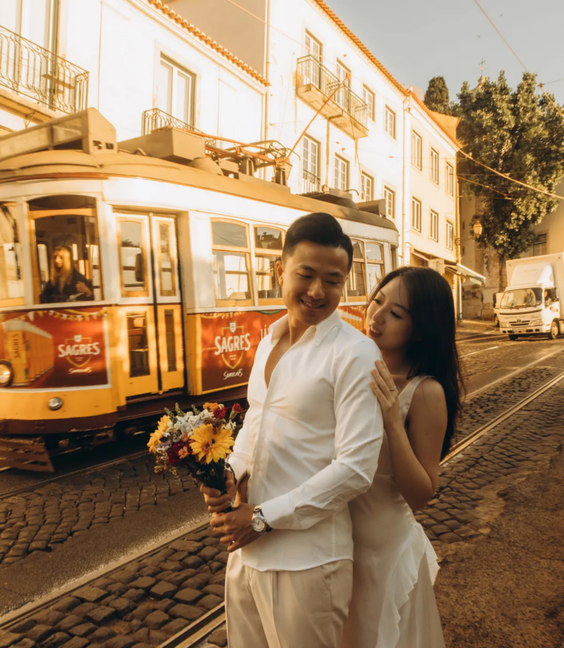 Couple with a bouquet beside a tram on a golden-lit Alfama street, Lisbon