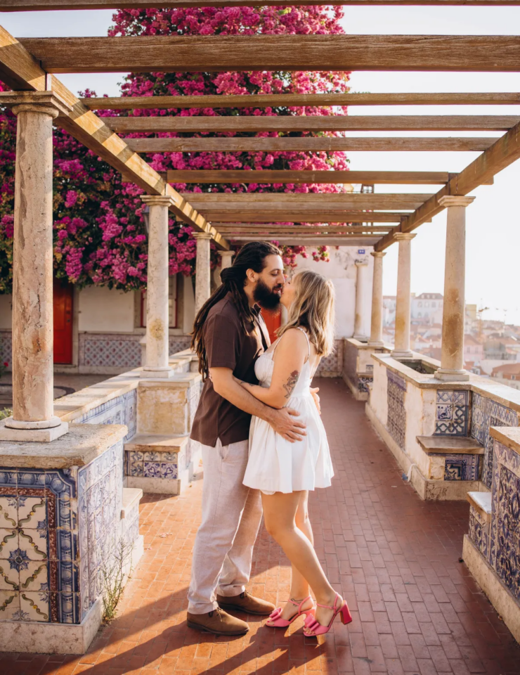 Couple kissing under the pink bougainvillea pergola at Miradouro de Santa Luzia, Lisbon