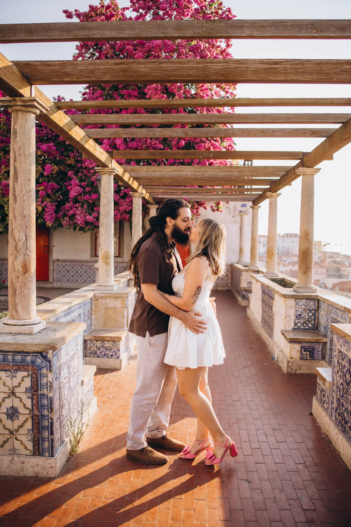 Couple kissing under the pink bougainvillea pergola at Miradouro de Santa Luzia, Lisbon