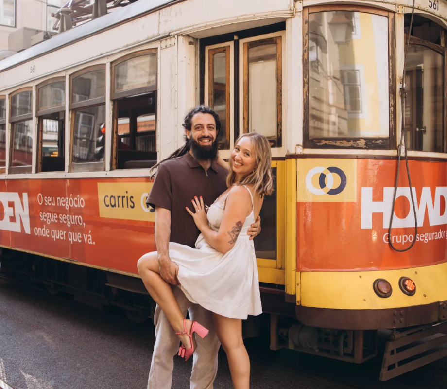 Man lifting his partner in front of a yellow vintage tram in Alfama, Lisbon
