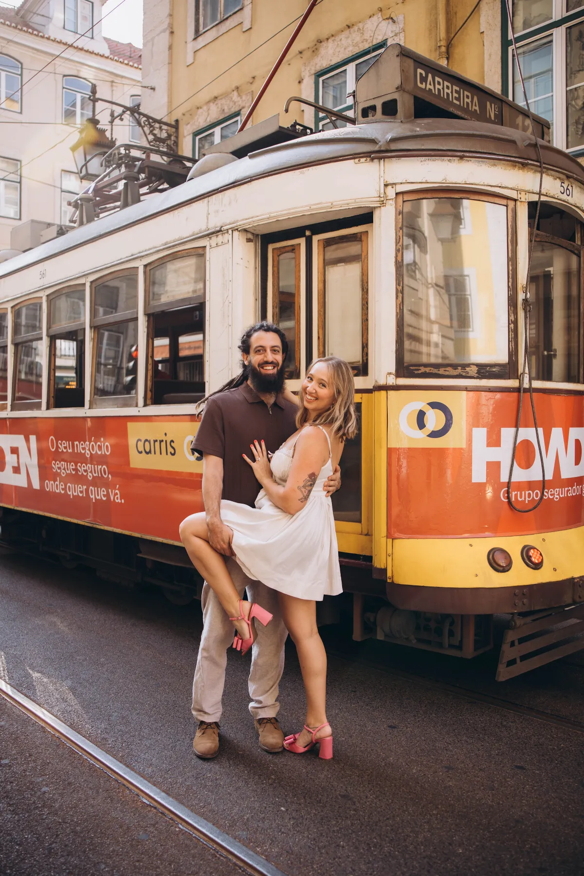 Man lifting his partner in front of a yellow vintage tram in Alfama, Lisbon