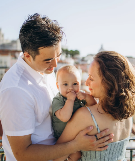 Parents cuddling their smiling baby above the terracotta rooftops of Alfama, Lisbon