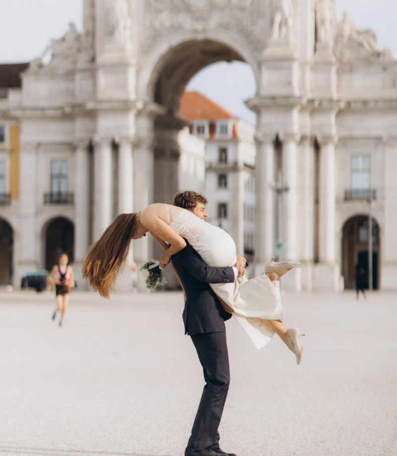 Groom lifting the bride in front of the Rua Augusta Arch on Praca do Comercio, Lisbon