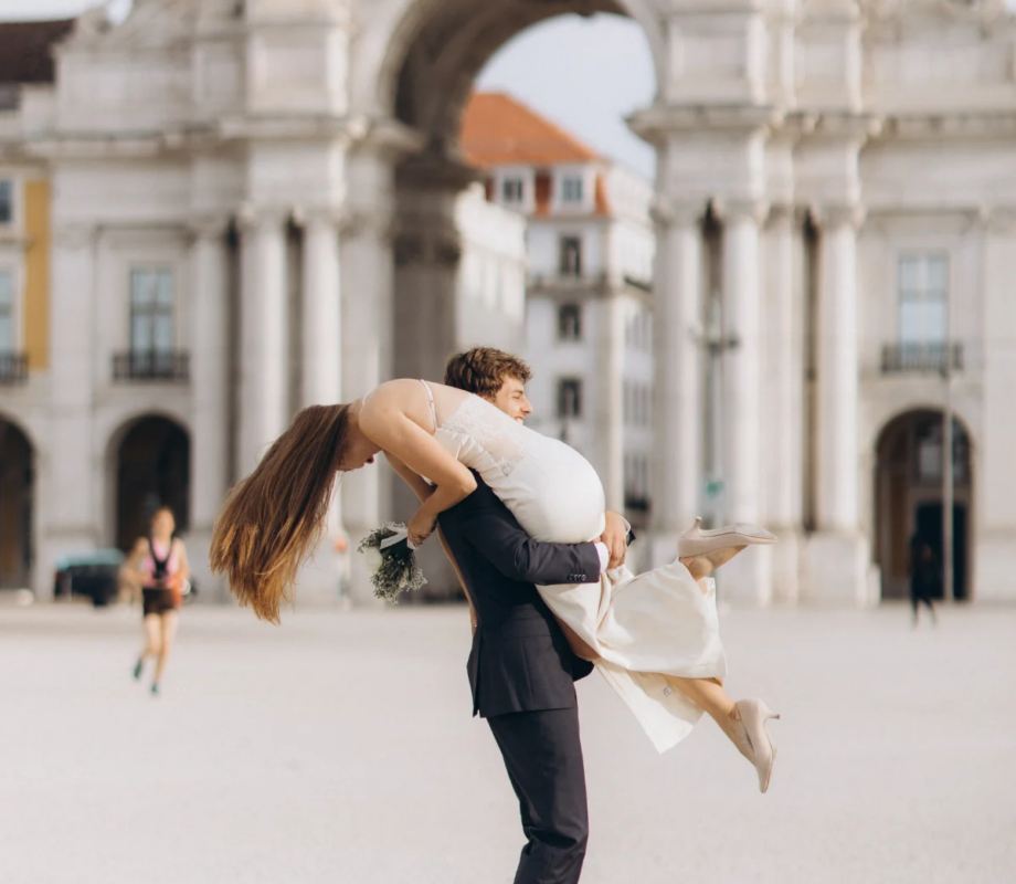 Groom lifting the bride in front of the Rua Augusta Arch on Praca do Comercio, Lisbon
