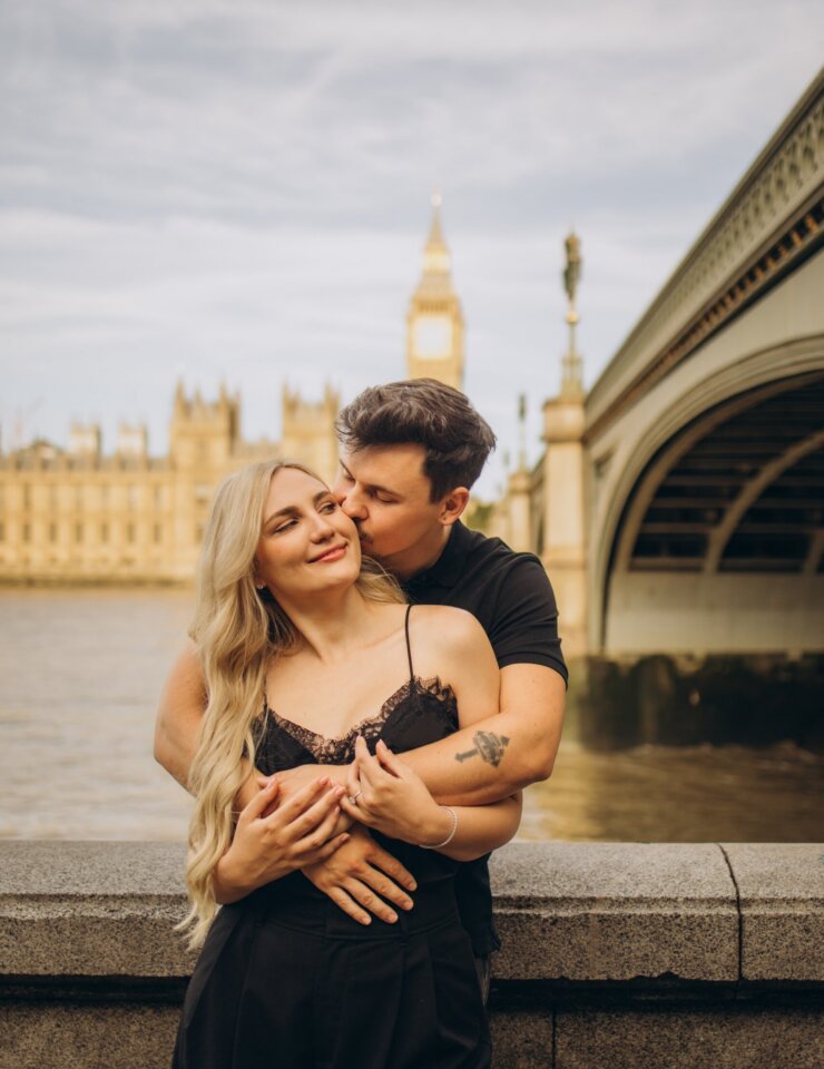 Man kissing his partner's cheek by Westminster Bridge in golden light, London