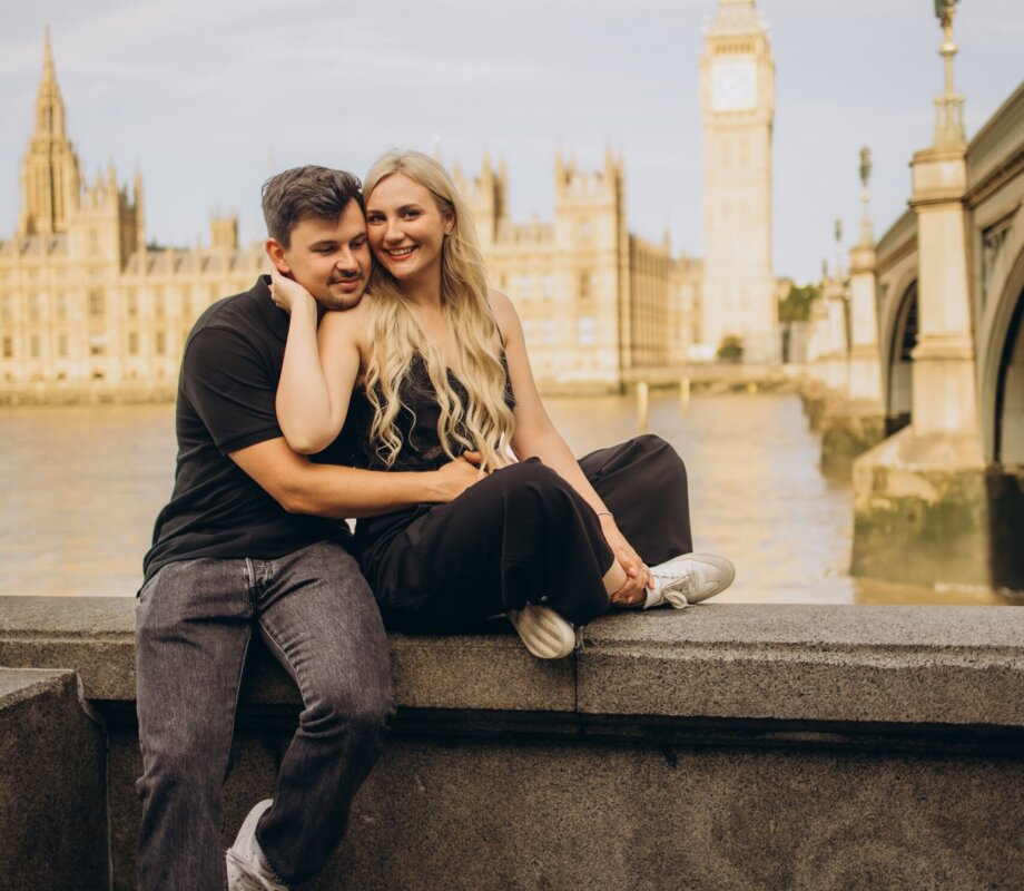 Couple relaxing on the river steps in warm sunlight with Big Ben and the Houses of Parliament behind, London