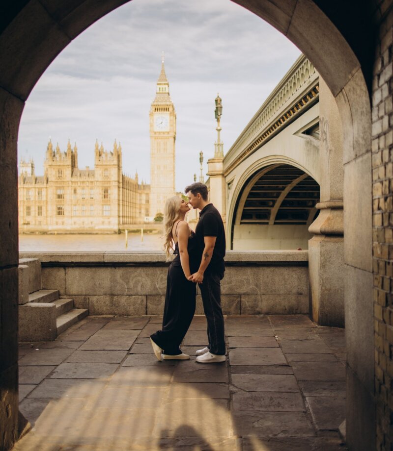 Couple kissing in the stone arch under Westminster Bridge, Big Ben framed behind, London