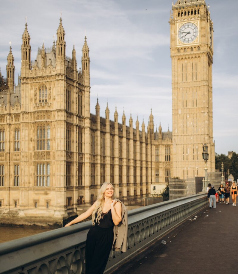 Woman leaning on Westminster Bridge in sunshine with Big Ben and Parliament behind, London