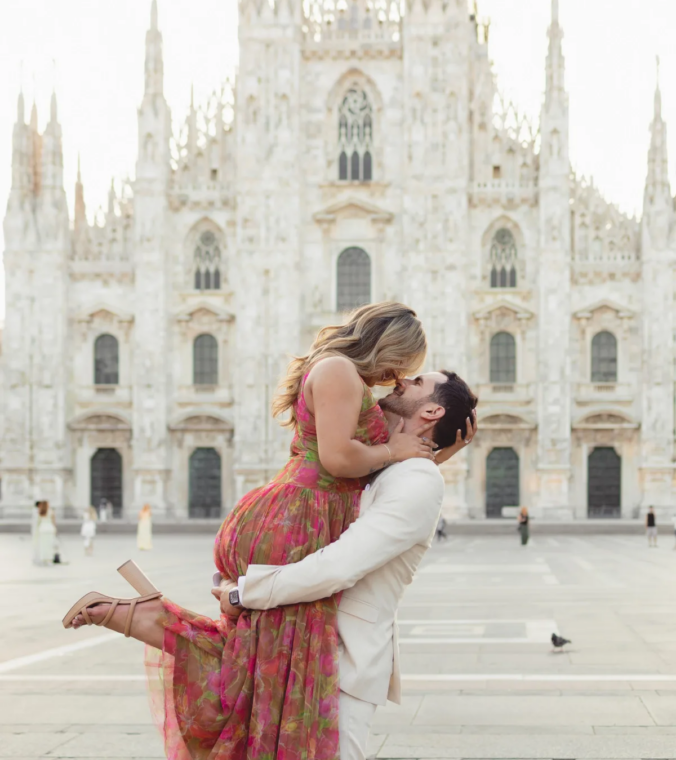 Man lifting his partner for a kiss on Piazza del Duomo, the cathedral behind, Milan