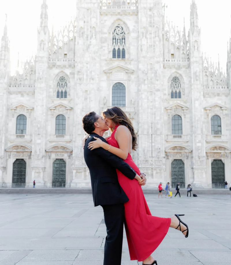 Man lifting his partner in a red dress mid-kiss on the open Duomo square, Milan