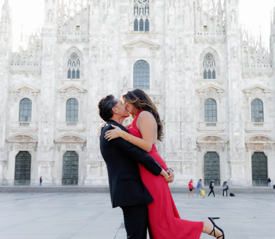 Man lifting his partner in a red dress mid-kiss on the open Duomo square, Milan