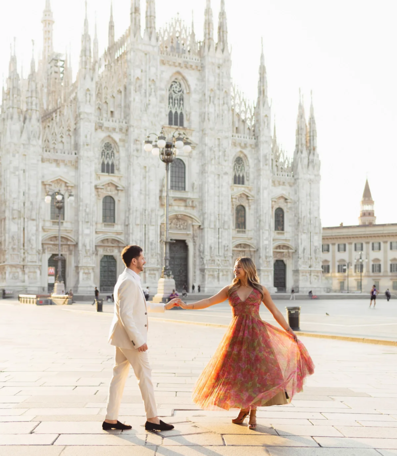 Pink dress flaring as he spins her across the sunlit Duomo square with long morning shadows, Milan