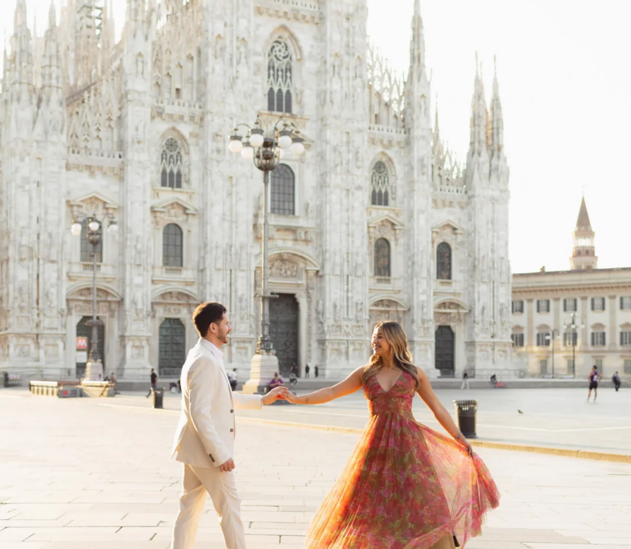 Pink dress flaring as he spins her across the sunlit Duomo square with long morning shadows, Milan