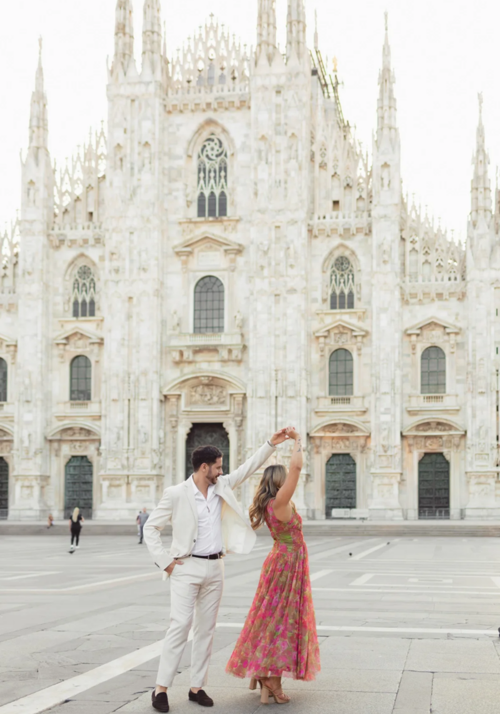 Man spinning his partner by the hand on the open Piazza del Duomo, the gothic cathedral facade behind, Milan