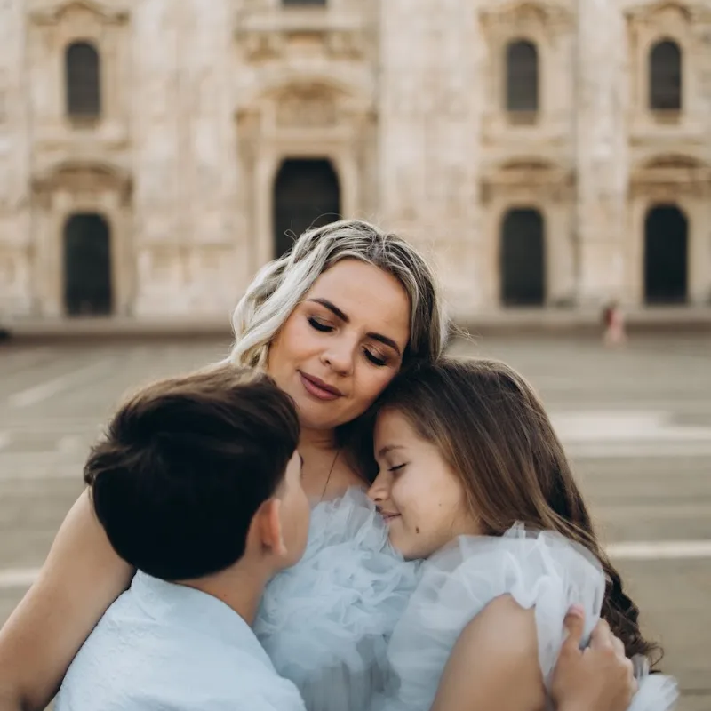 Mother in a tulle dress hugging her two children at the Duomo, Milan