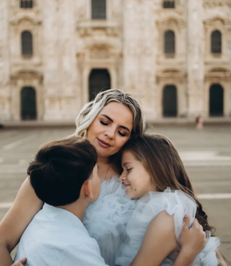Mother in a tulle dress hugging her two children at the Duomo, Milan