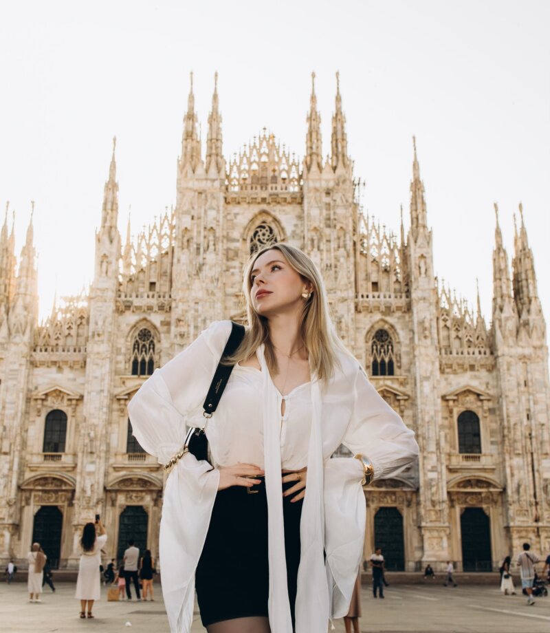 Woman in a white blouse glancing up toward the spires of Milan Cathedral, Milan