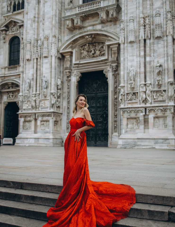 Woman in a strapless red gown smiling on the Duomo steps, her train draped over the stairs, Milan