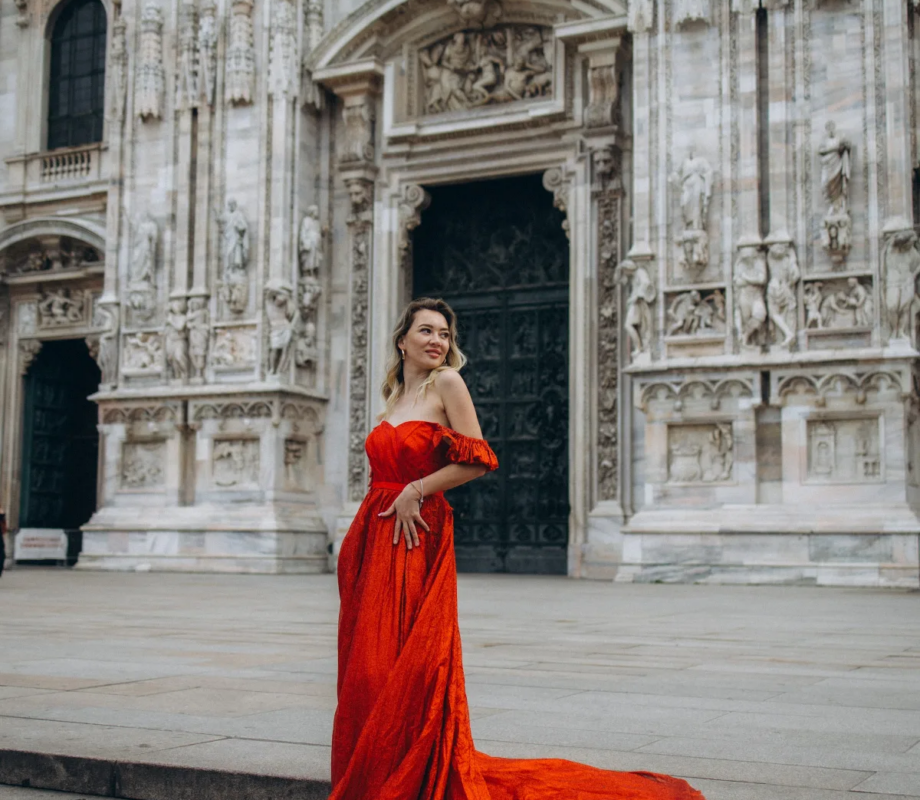 Woman in a strapless red gown smiling on the Duomo steps, her train draped over the stairs, Milan