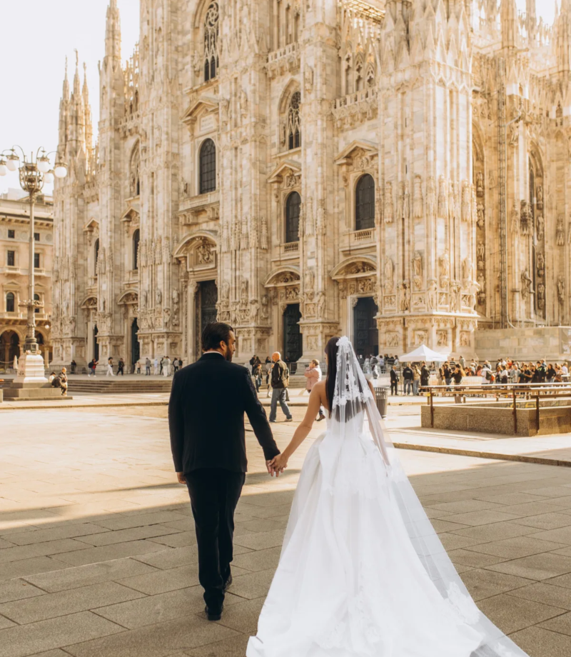 Groom leading the bride by the hand toward the Duomo, her cathedral-length veil trailing, Milan