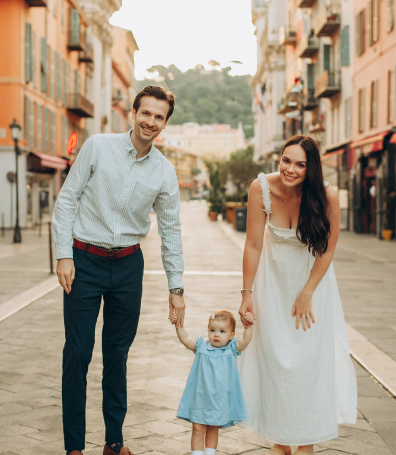 Parents walking hand in hand with their toddler down a pastel street in Vieux Nice